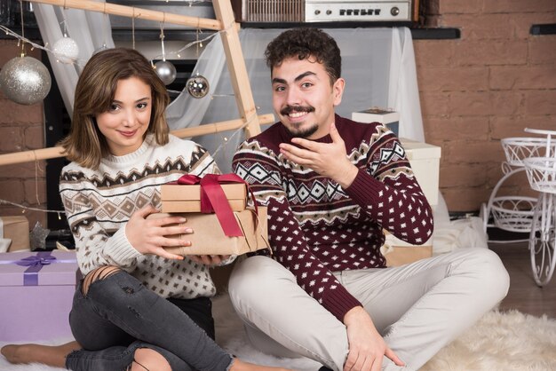 Junges Paar sitzt mit Weihnachtsgeschenken in der Nähe von festlichen silbernen Kugeln.