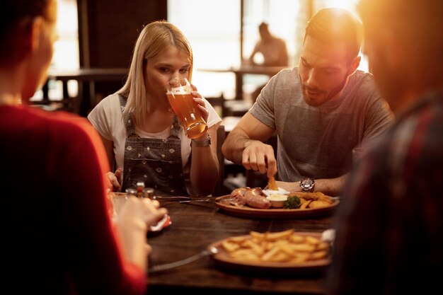 Junges Paar trifft sich mit Freunden in einem Pub und genießt Bier und Essen