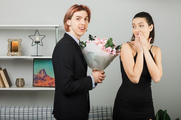 Junges Paar umarmte sich am glücklichen Frauentag mit Blumenstraußfrauenflüsterungen, die im Wohnzimmer stehen