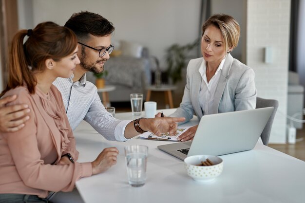 Junges Paar und Immobilienmakler mit Laptop bei einem Meeting im Büro