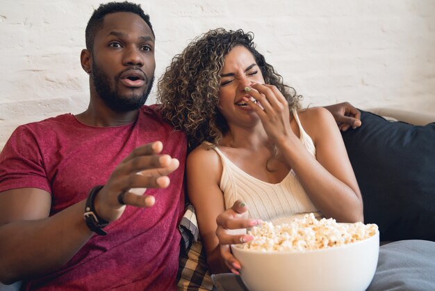 Junges Paar verbringt Zeit zusammen und schaut sich Fernsehserien oder Filme an, während es zu Hause auf der Couch sitzt.