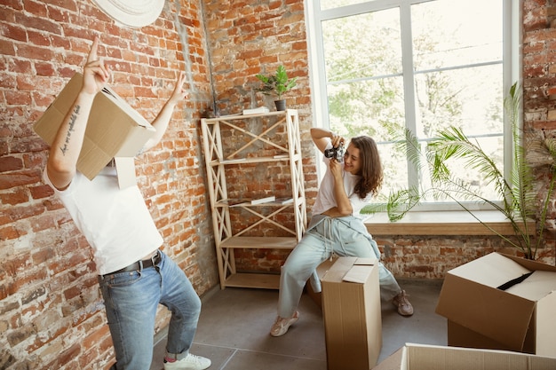 Junges Paar zog in ein neues Haus oder eine neue Wohnung. Spaß mit Pappkartons haben, nach dem Reinigen und Auspacken am Umzugstag entspannen