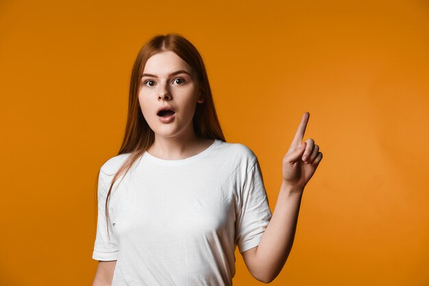 Junges Redheadmädchen hat Blick überrascht und zeigt einen Finger beiseite oben