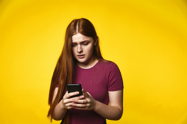 Junges Rothaarigemädchen hat Blick beim Schauen in ihrem Telefon gesorgt