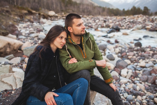 Junges schönes Hipster-Paar verliebt, am Fluss sitzend, wilde Natur, Winterferien