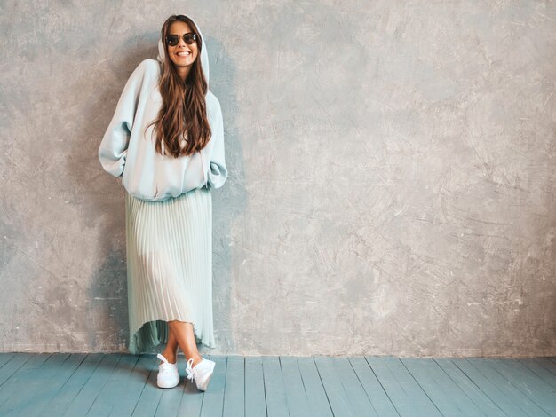 Junges schönes lächelndes Frauenschauen. Modisches Mädchen in der zufälligen Sommer Hoodie- und -rockkleidung. in Sonnenbrillen