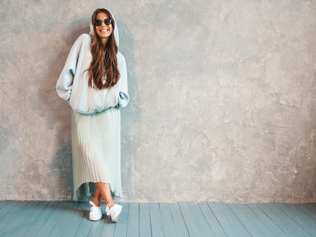 Junges schönes lächelndes Frauenschauen. Modisches Mädchen in der zufälligen Sommer Hoodie- und -rockkleidung. in Sonnenbrillen