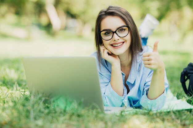 Junges schönes lächelndes Modell unter Verwendung des neuen Laptops im Stadtpark am sonnigen Tag