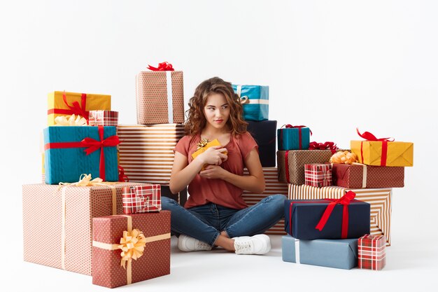 Junges schönes lockiges Mädchen, das auf Boden unter Geschenkboxen lokalisiert sitzt