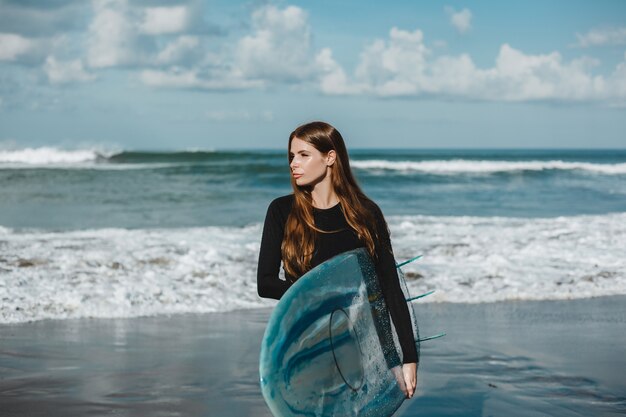 junges schönes Mädchen, das auf dem Strand mit einem Surfbrett, Frauensurfer, Meereswogen aufwirft