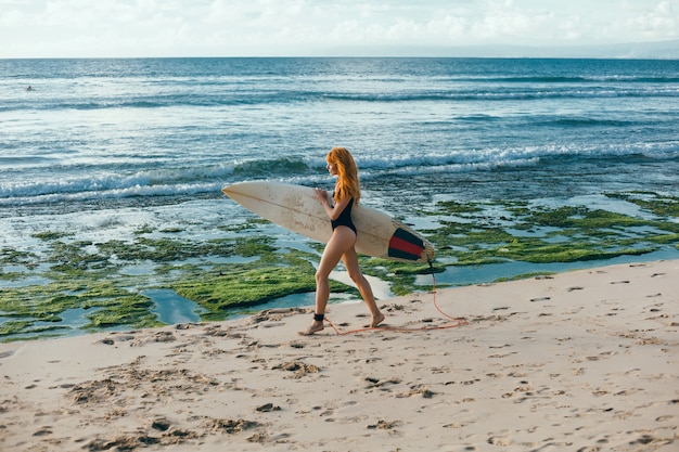 Kostenloses Foto junges schönes mädchen, das auf dem strand mit einem surfbrett, frauensurfer, meereswogen aufwirft