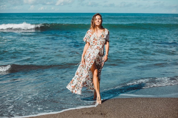 junges schönes Mädchen, das auf dem Strand, Ozean, Wellen, heller Sonne und gebräunter Haut aufwirft