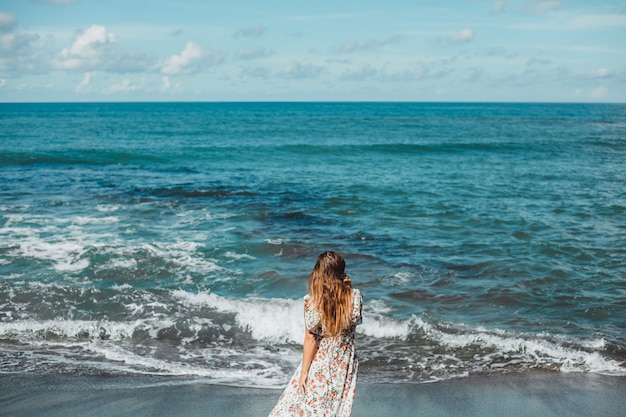 junges schönes Mädchen, das auf dem Strand, Ozean, Wellen, heller Sonne und gebräunter Haut aufwirft