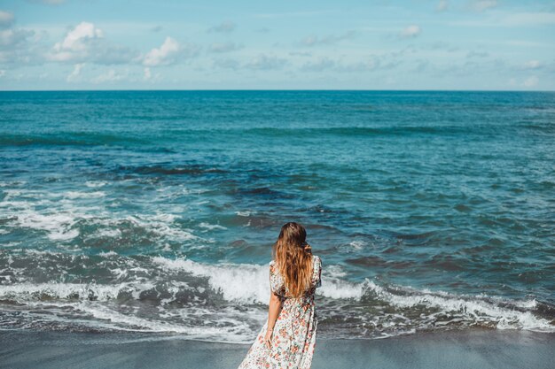 junges schönes Mädchen, das auf dem Strand, Ozean, Wellen, heller Sonne und gebräunter Haut aufwirft