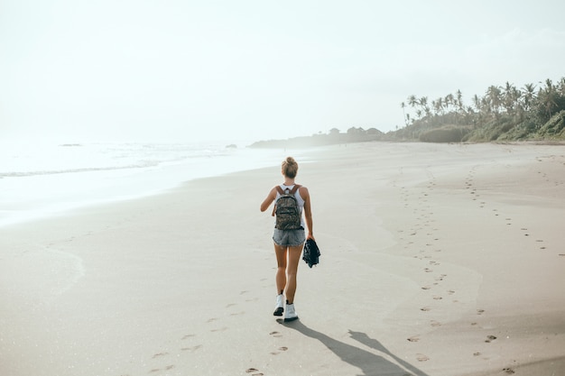 junges schönes Mädchen, das auf dem Strand, Ozean, Wellen, heller Sonne und gebräunter Haut aufwirft