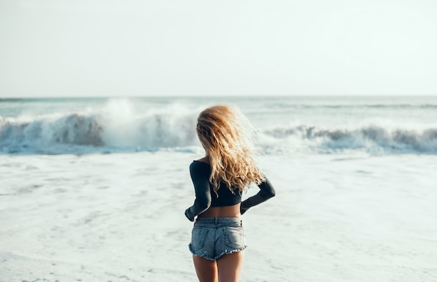 junges schönes Mädchen, das auf dem Strand, Ozean, Wellen, heller Sonne und gebräunter Haut aufwirft