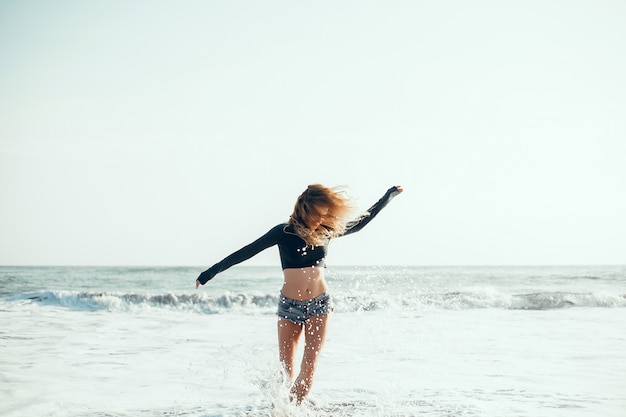 junges schönes Mädchen, das auf dem Strand, Ozean, Wellen, heller Sonne und gebräunter Haut aufwirft