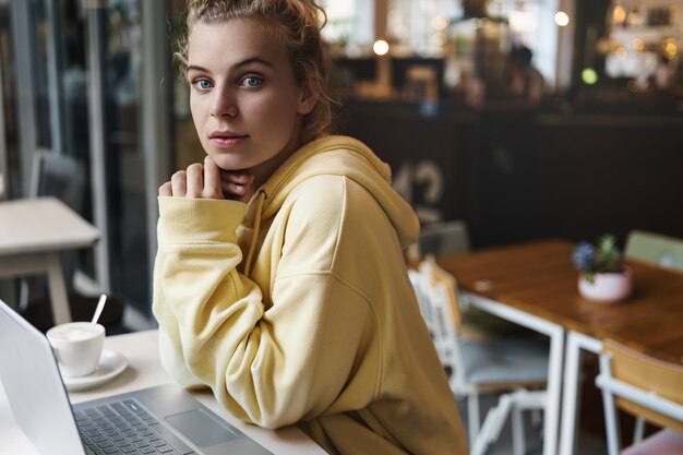 Junges schönes Mädchen, das in einem Café mit Laptop sitzt. Studentin, die am Coffeeshop studiert.