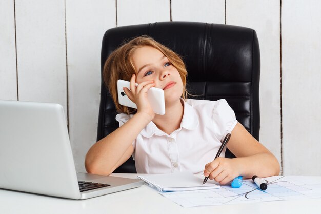 Junges schönes Mädchen, das Telefon am Arbeitsplatz im Büro spricht.