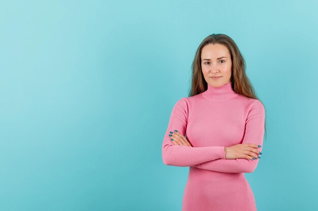 Junges schönes Mädchen schaut in die Kamera, indem sie die Arme auf blauem Hintergrund kreuzt