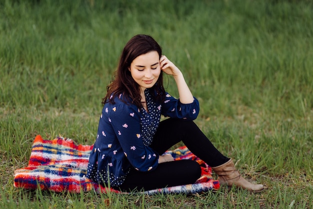 Junges schönes Mädchen sitzt auf einem Plaid im Frühlingspark