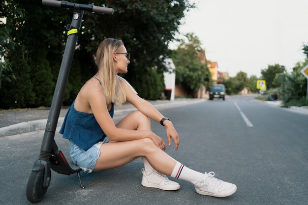 Junges schönes Mädchen sitzt auf ihrem Elektroroller im Sommer auf der Straße