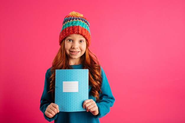 Junges schönes Mädchen, welches das blaue Exemplarbuch und -c $ lächeln getrennt zeigt
