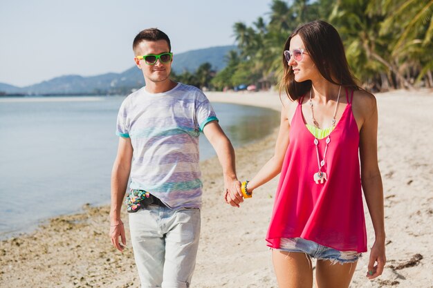 Junges schönes Paar, das auf tropischem Strand in Thailand geht, Händchen haltend, lächelnd, glücklich, Spaß habend, Sonnenbrille, Hipster-Outfit, lässiger Stil, Honigmond, Urlaub, Sommerzeit, sonnig