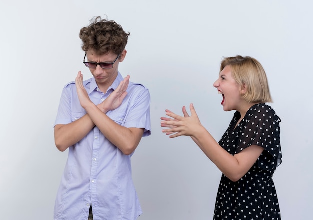 Junges schönes Paar, das Frau streit, die auf ihrem Freund schreit, der Stoppgeste mit hfrowning Gesicht über weißer Wand zeigt