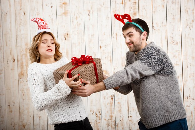 Junges schönes Paar, das für Weihnachtsgeschenk über Holzwand kämpft