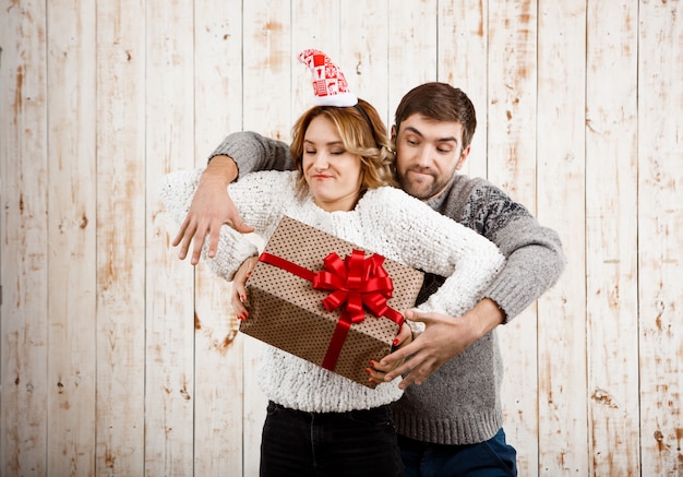 Junges schönes Paar, das für Weihnachtsgeschenk über Holzwand kämpft