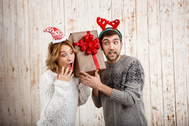 Junges schönes Paar, das Weihnachtsgeschenk über Holzwand hält