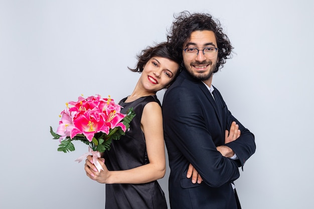 Junges schönes Paar glücklicher Mann und Frau mit Blumenstrauß, die fröhlich lächelnd in der Liebe zum Valentinstag aussehen