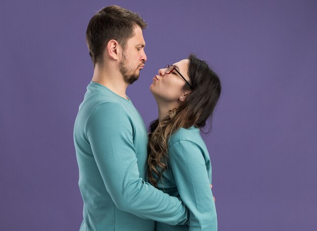 Junges schönes Paar in blauer Freizeitkleidung glücklicher und fröhlicher Mann und Frau, die sich umarmen, um sich glücklich zu küssen