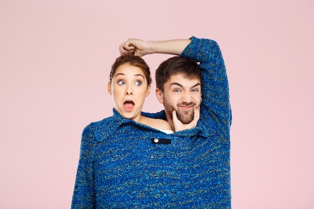 Kostenloses Foto junges schönes paar in einem blauen strickpullover posierend lächelnd, der spaß über hellrosa wand hat