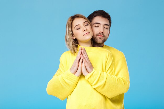 Junges schönes Paar in einem gelben Pullover, der lächelnd über blaue Wand umarmt