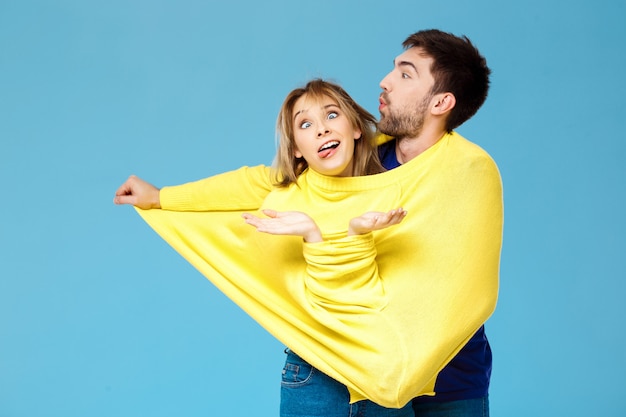 Junges schönes Paar in einem gelben Pullover posierend lächelnd, der Spaß über blauer Wand hat