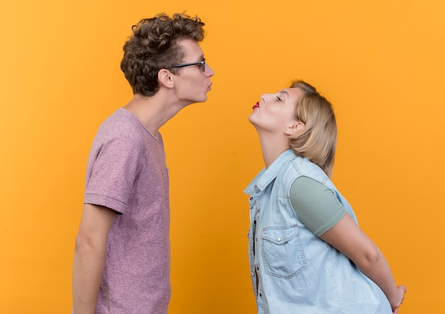 Junges schönes Paar Mann und Frau glücklich in der Liebe, die Lippen hält, wie sie sich küssen, die über orange Wand stehen