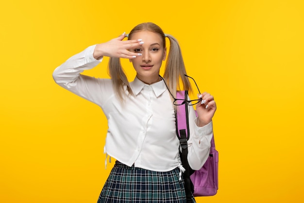 Junges Schulmädchen des Weltbuchtages, das Gesicht mit der Hand auf gelbem Hintergrund bedeckt