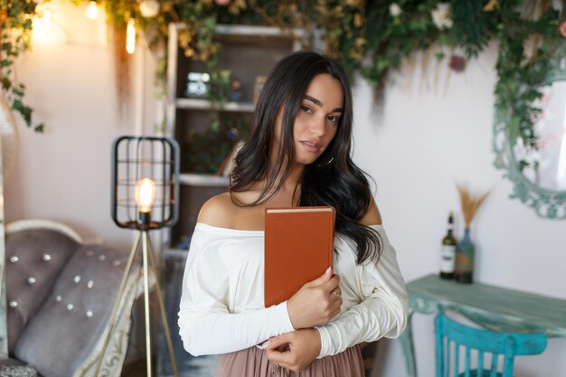 Junges selbstbewusstes Mädchen umarmte ihr Buch und schaute in die Kamera Hochwertiges Foto