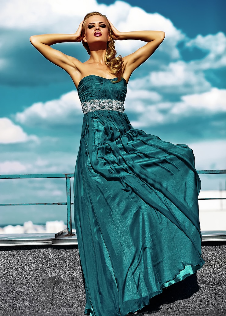Kostenlose Foto junges sexy blondes frauenmodell im abendkleid, das auf hintergrund des blauen himmels aufwirft