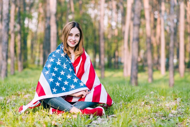 Junges Sitzen auf der Grundfrau, die in der amerikanischen Flagge einwickelt