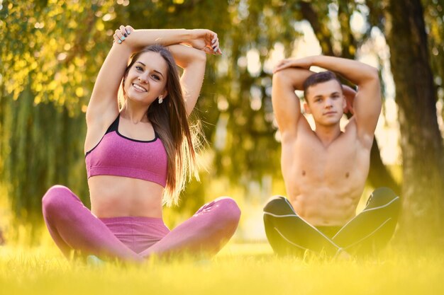 Junges sportliches Paar, das sich nach Fitness- und Yoga-Übungen auf einer Wiese in einem Park entspannt.