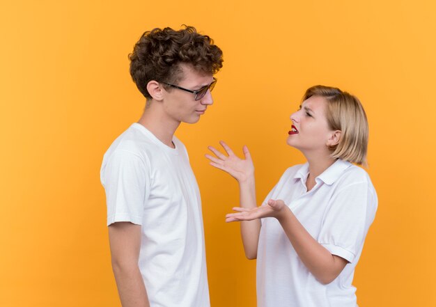 Junges sportliches Paar Mann und Frau, die einander streitend und streitend betrachten, die über orange Wand stehen