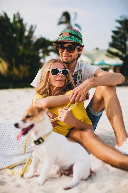 Junges stilvolles Hipster-Paar in der Liebe zu Fuß spielen Hund Welpe Jack Russell, tropischer Strand, cooles Outfit, romantische Stimmung, Spaß haben, sonnig, Mann Frau zusammen, horizontal, Urlaub, Haus zu Hause Villa