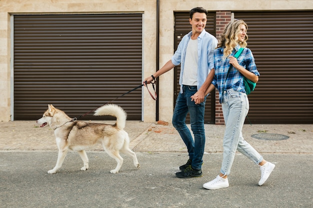 Junges stilvolles Paar, das mit Hund in Straße geht. Mann und Frau glücklich zusammen mit Husky Rasse