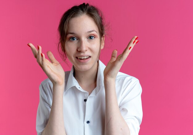 Junges überraschtes blondes russisches Mädchen hält Hände nahe Gesicht auf Rosa mit Kopienraum