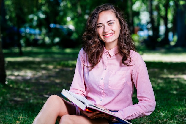 Junges weibliches Sitzen im Park mit Buch