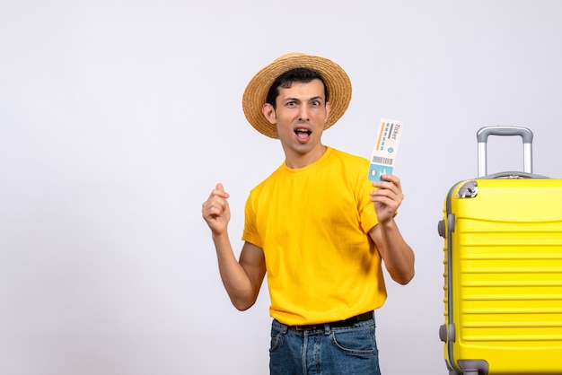 Jungtourist der Vorderansicht im gelben T-Shirt, das nahe gelbem Koffer hält, der Ticket hält