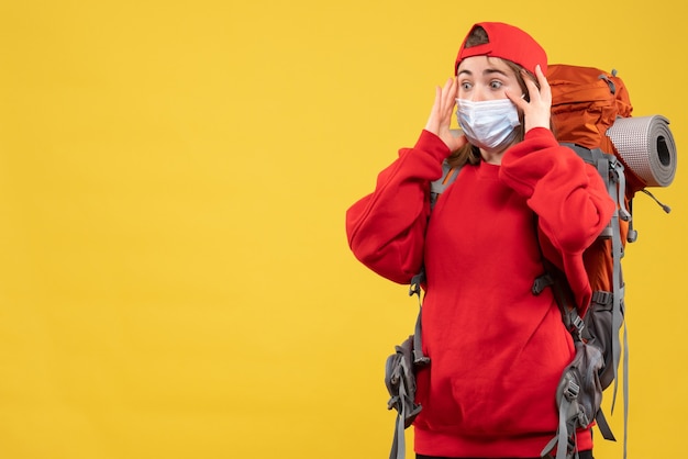 Jungtourist der vorderansicht mit großen augen mit touristenrucksack und maskenhaltekopf